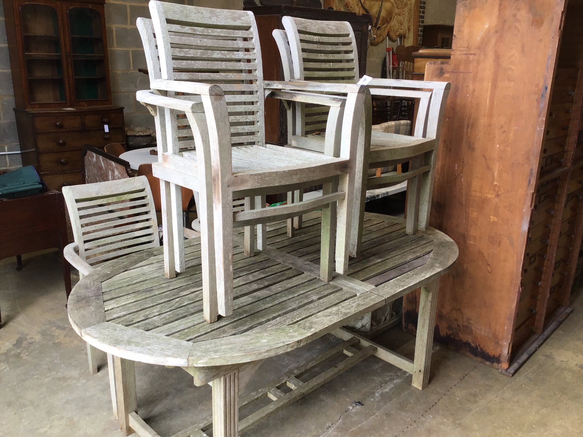 A weathered teak oval extending garden table, 242 cm extended, width 102 cm, height 73 cm and six stacking elbow chairs.